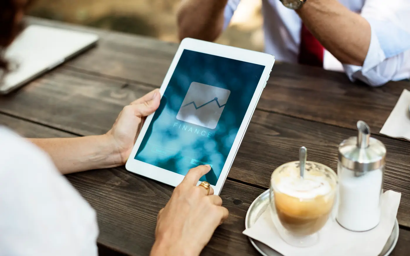 Two hands holding a tablet with a chart on it, beside a cup of coffee