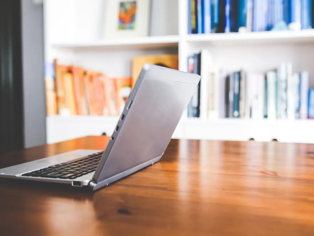 A laptop open on a desk in front of bookshelves